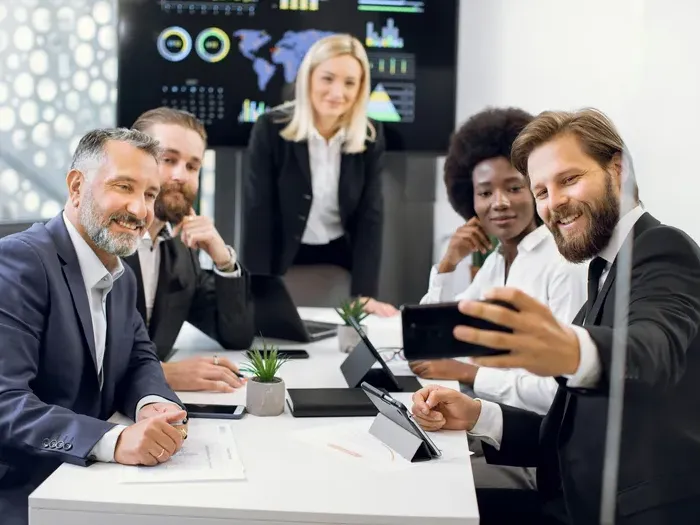 Group of professionals in formal wear smiling and taking a selfie during a meeting in a modern office setting